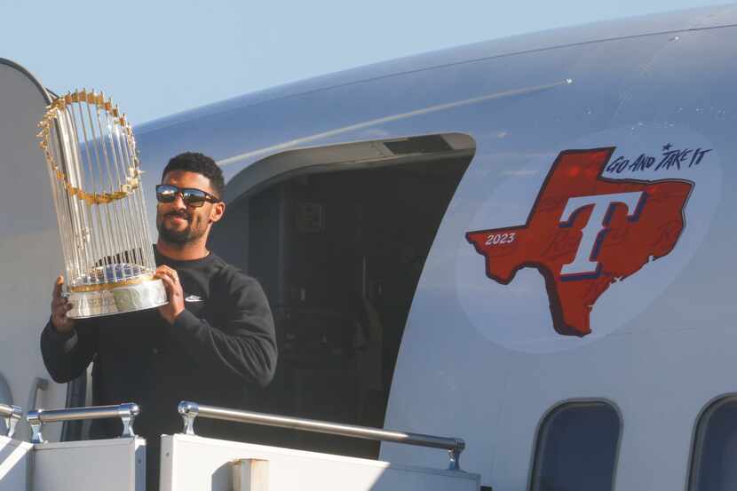 Texas Rangers’ Marcus Semien hoists the commissioner's trophy upon the arrival of the team...