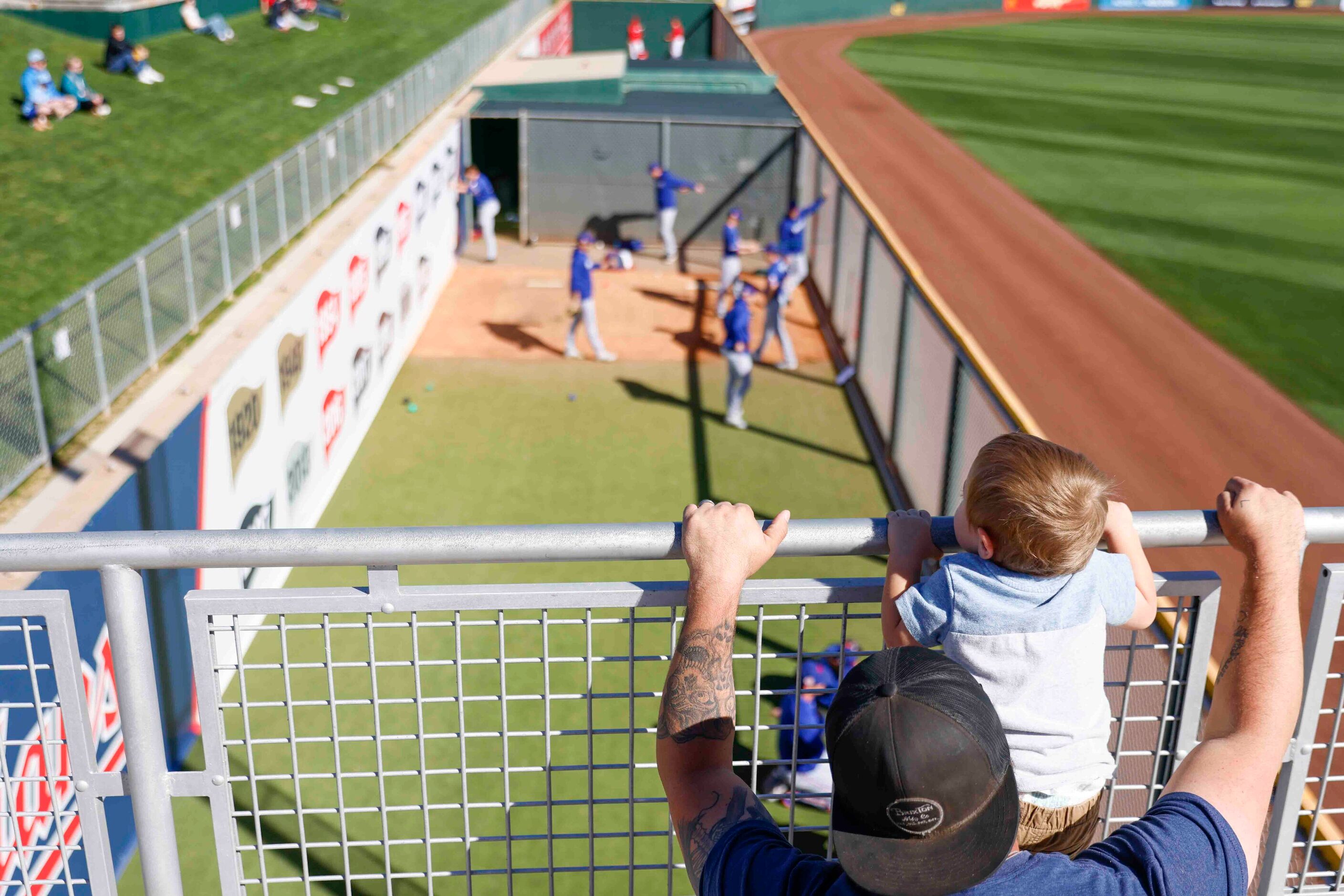 Maverick Hackett, 2, with his father Jacob, leans on the railing to watch Texas Rangers warm...