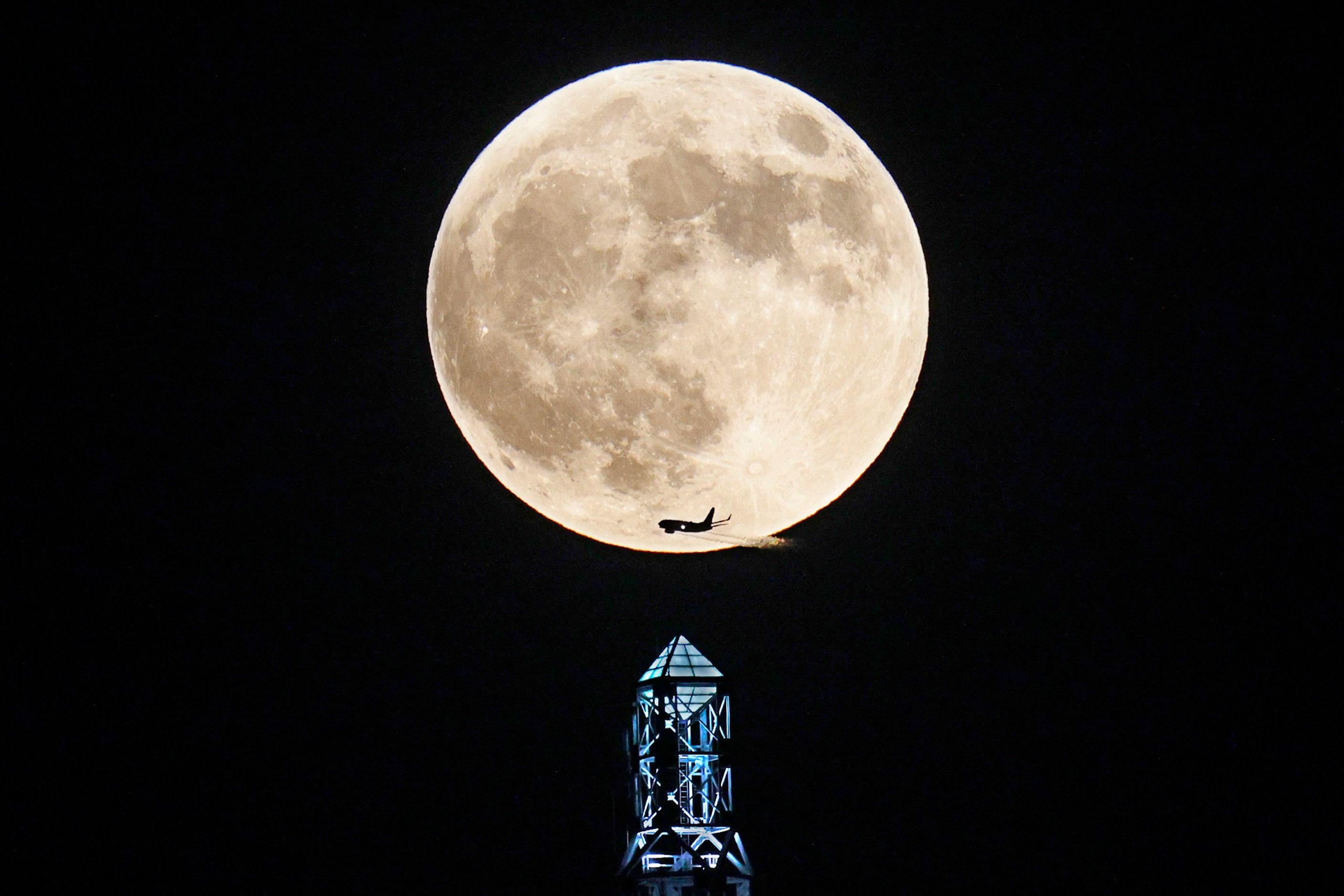 The full moon rises above Renaissance Tower as an airplane crosses in front of the moon,...