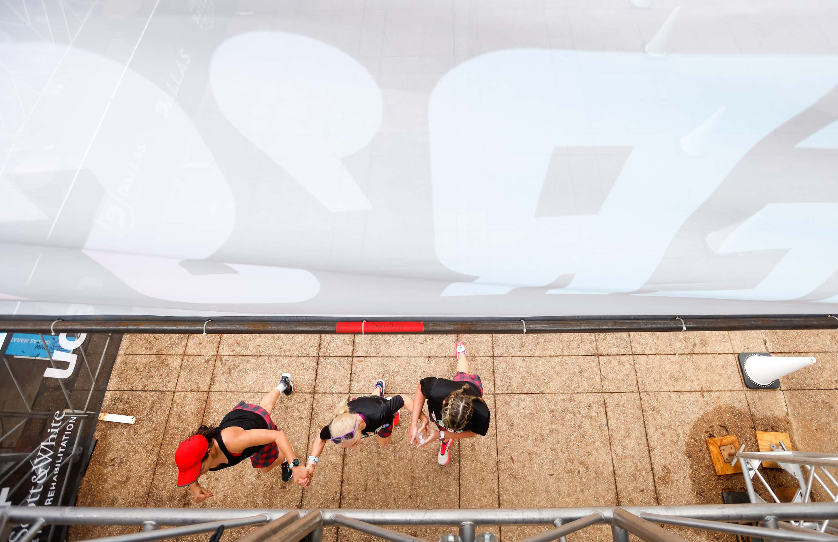 Three half-marathon runners hold hands as they near the finish line of the BMW Dallas...