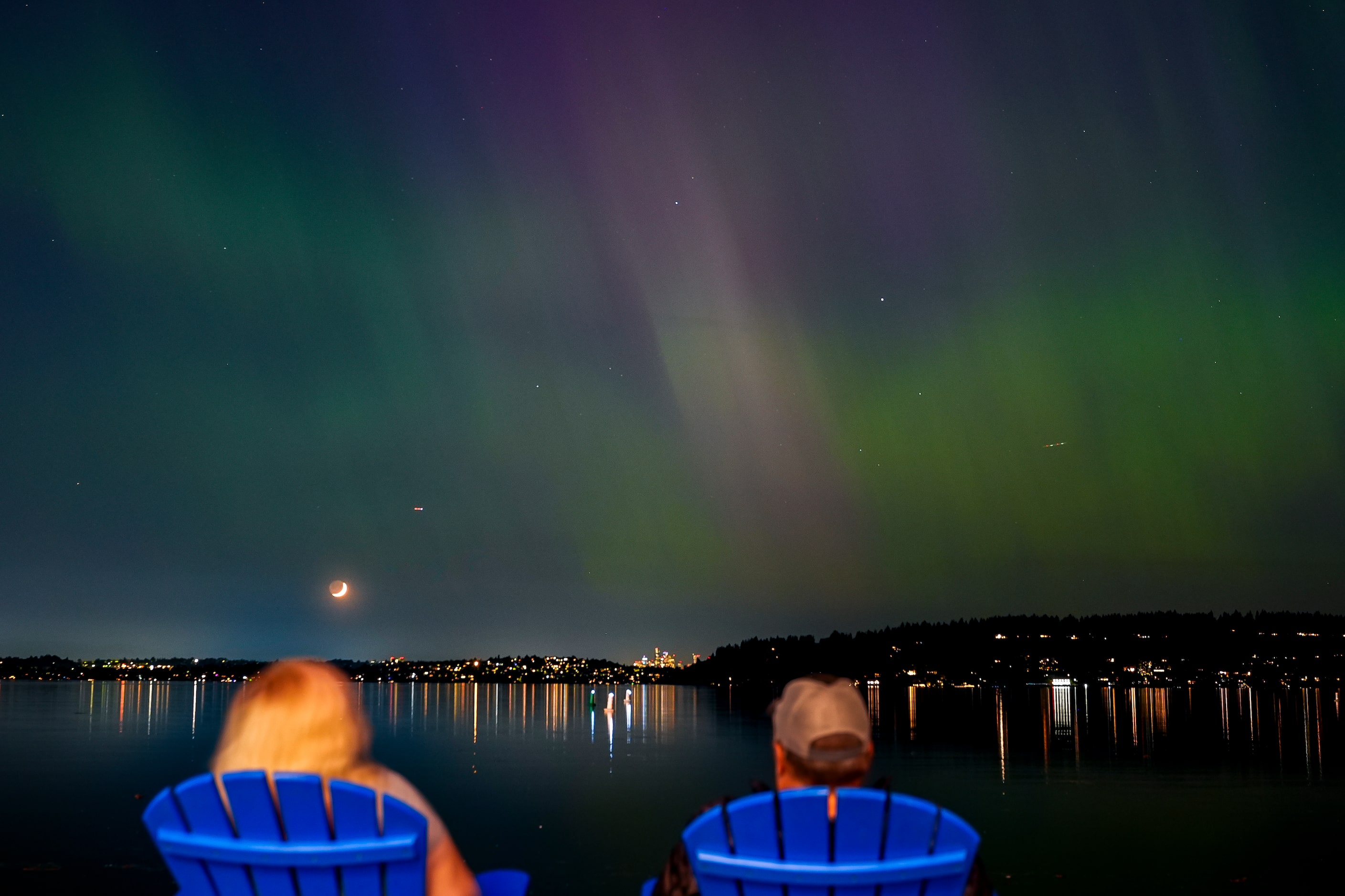 People view the northern lights, or aurora borealis, as they glow over Lake Washington, in...