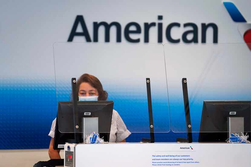 An American Airlines agent works behind a plexiglass barrier at a check in counter at Dallas...