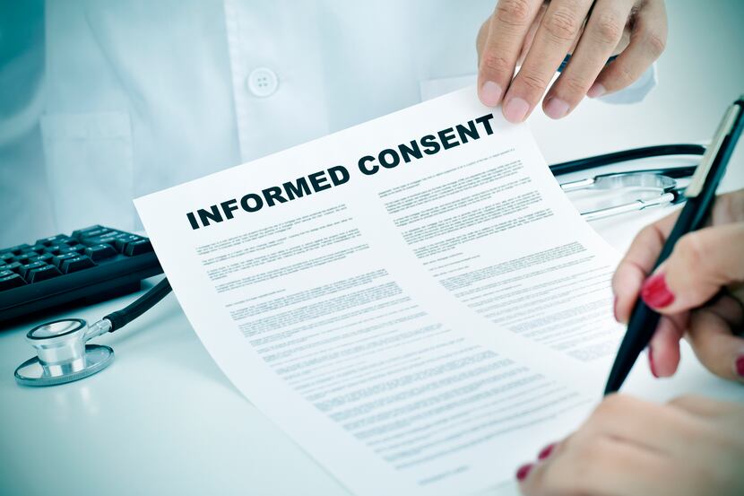Closeup of a young woman patient signing an informed consent document at the doctor's office.