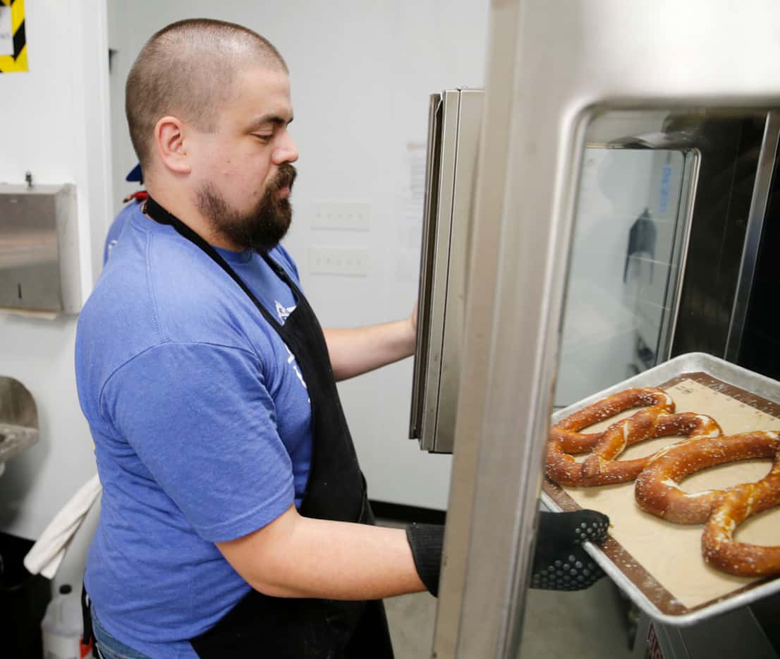 Travis Birge, the chief pretzel officer pulls, out some finished pretzels from the oven at...