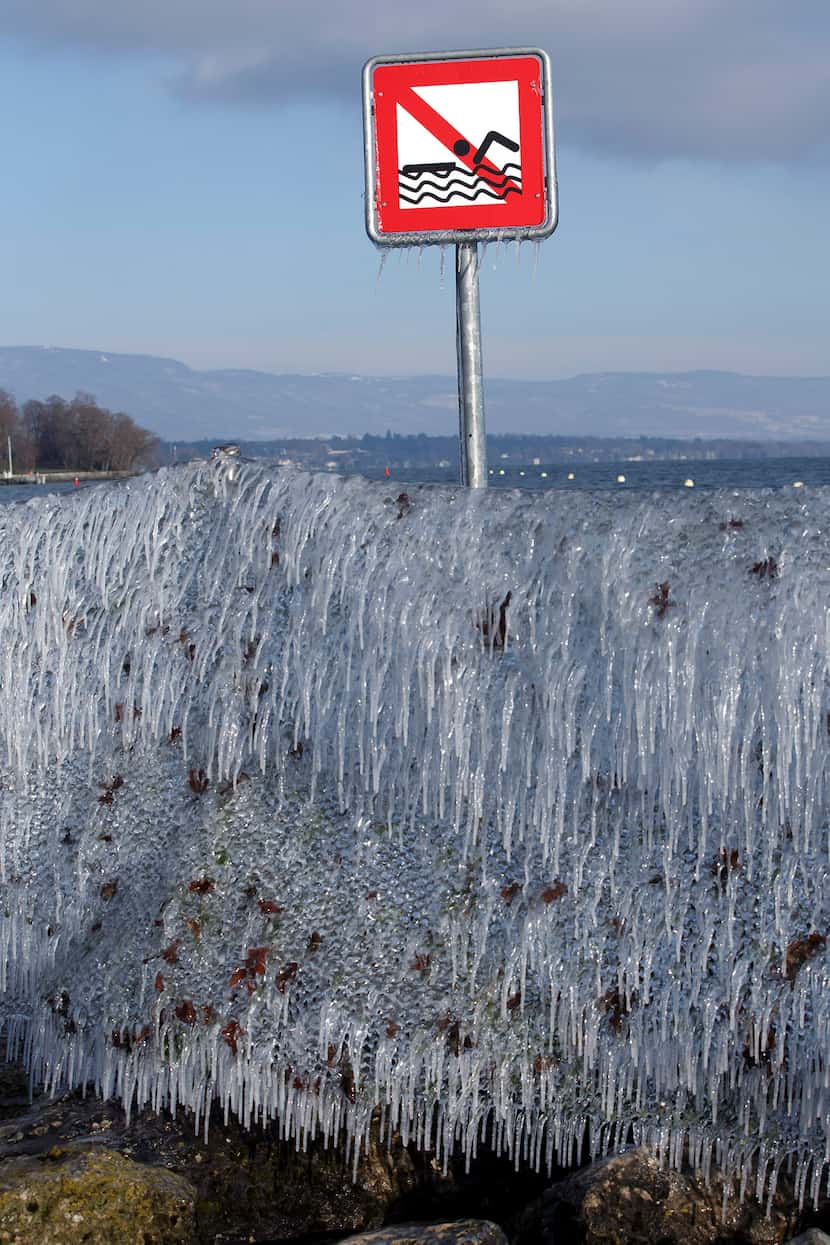  A ''no swimming'' signpost stands behind a fence covered with ice after the wind blew waves...