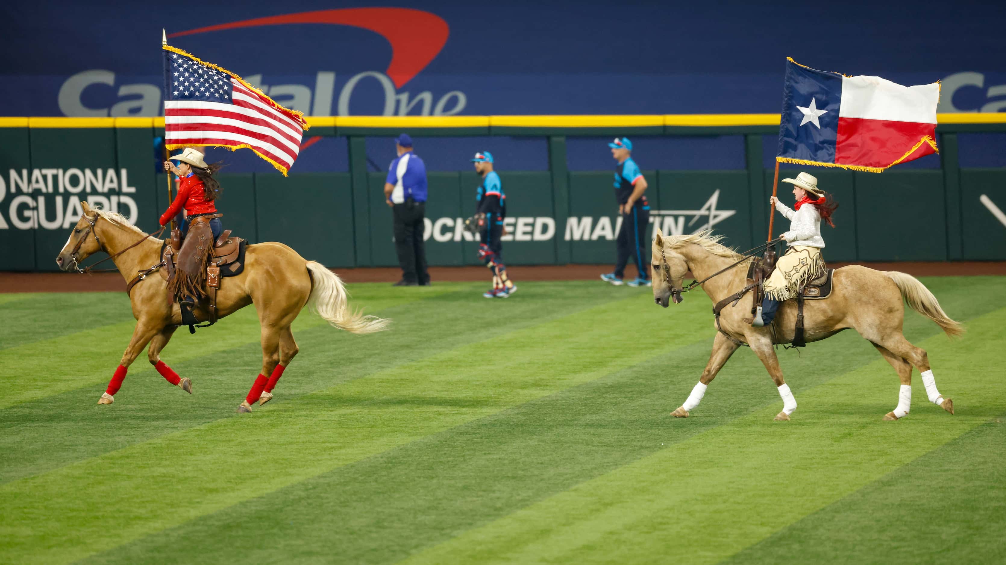 Women carry the American and Texas flags on horseback across the outfield before the MLB...