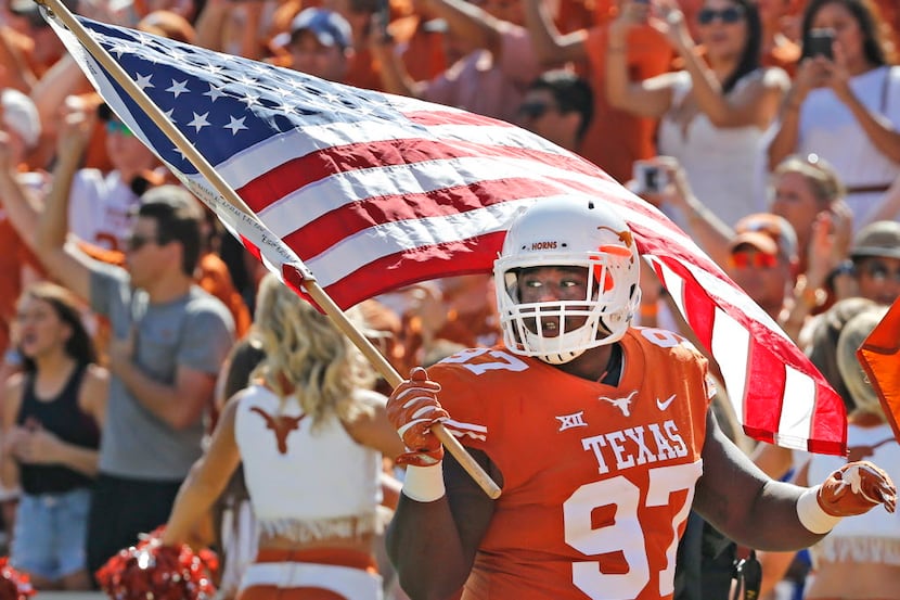 Texas Longhorns defensive lineman Chris Nelson (97) carries the American flag onto the field...
