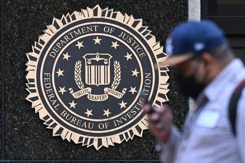 A pedestrian walks past a seal reading "Department of Justice Federal Bureau of...