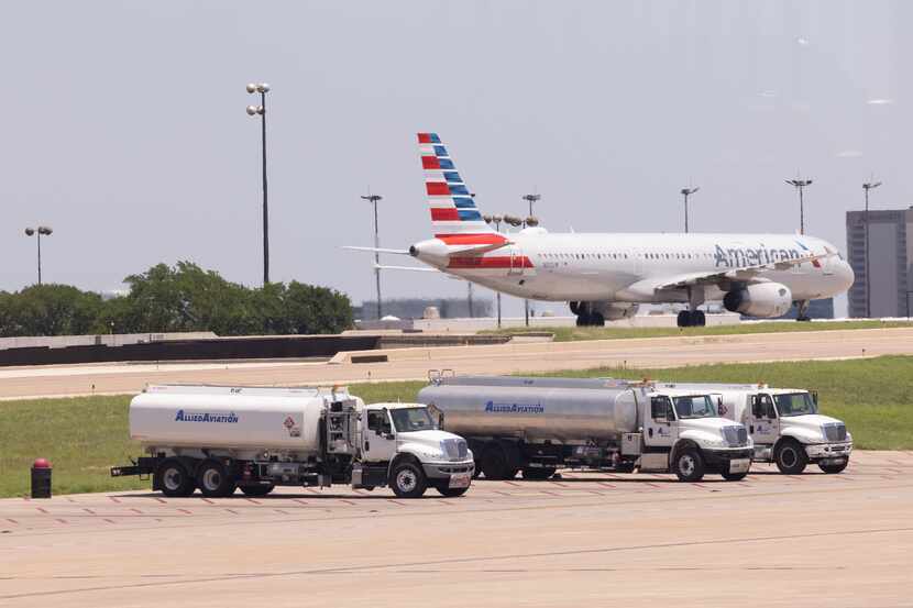 Fuel trucks sit in the foreground as an American Airlines plane taxis the runway at DFW...