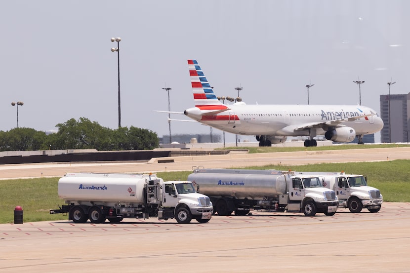 Fuel trucks sit in the foreground as an American Airlines plane taxis the runway at DFW...