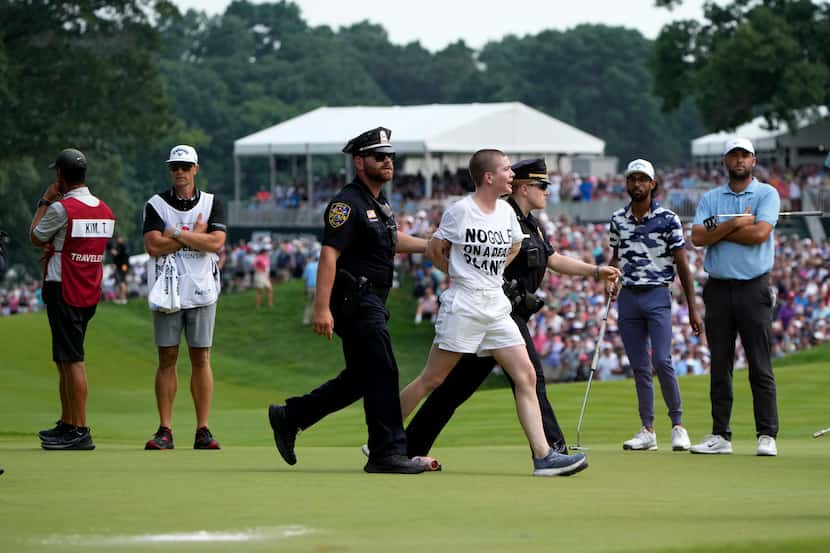 One of several protesters is led away after they ran onto the course on at the 18th hole as...