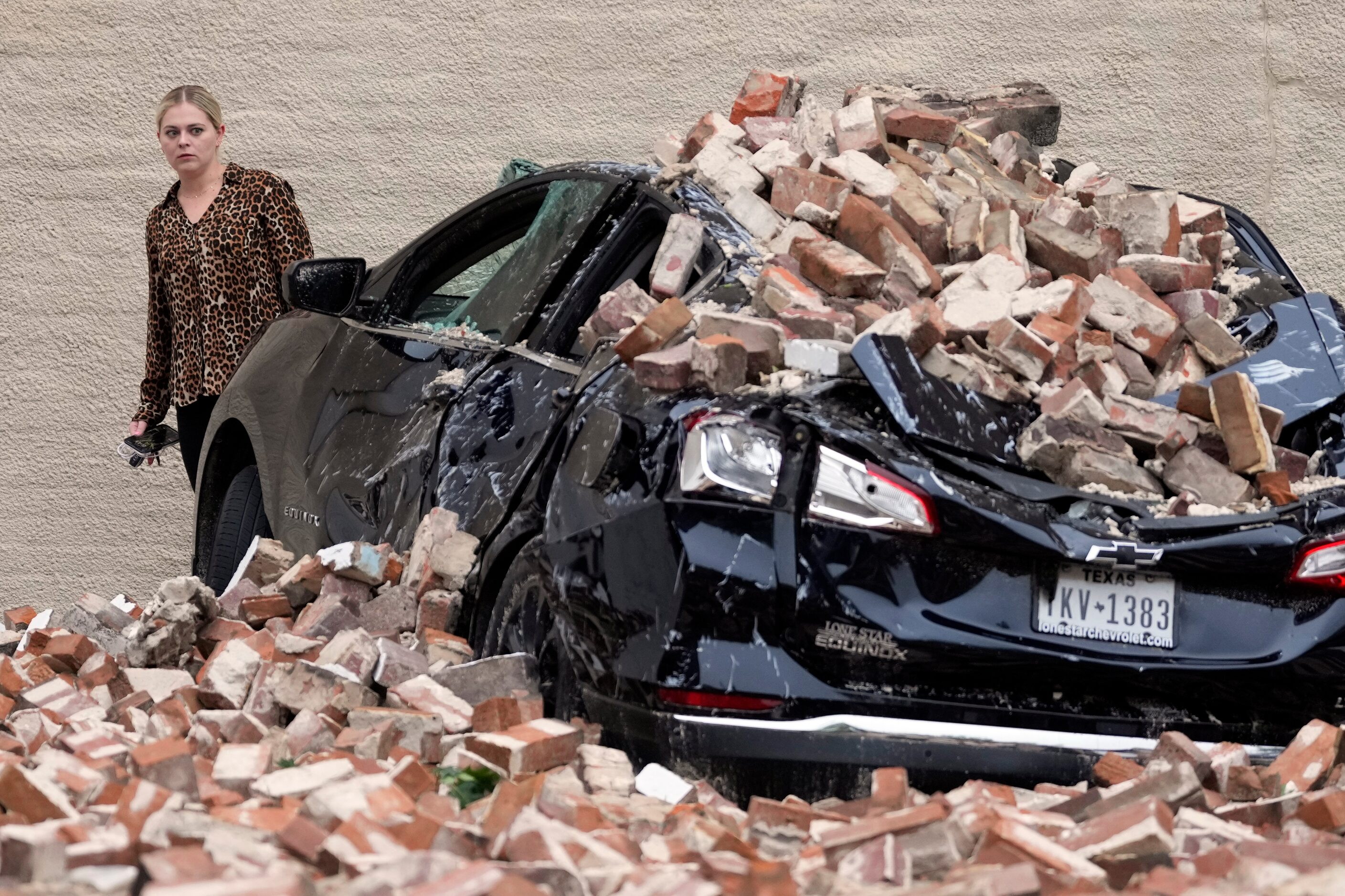 A woman looks at the damage caused by fallen bricks from a building wall in the aftermath of...