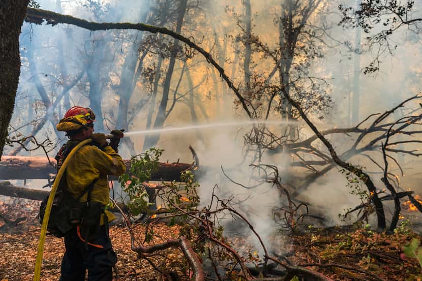 A firefighter sprays water on the Park Fire burning near Forest Ranch, Calif., Saturday,...