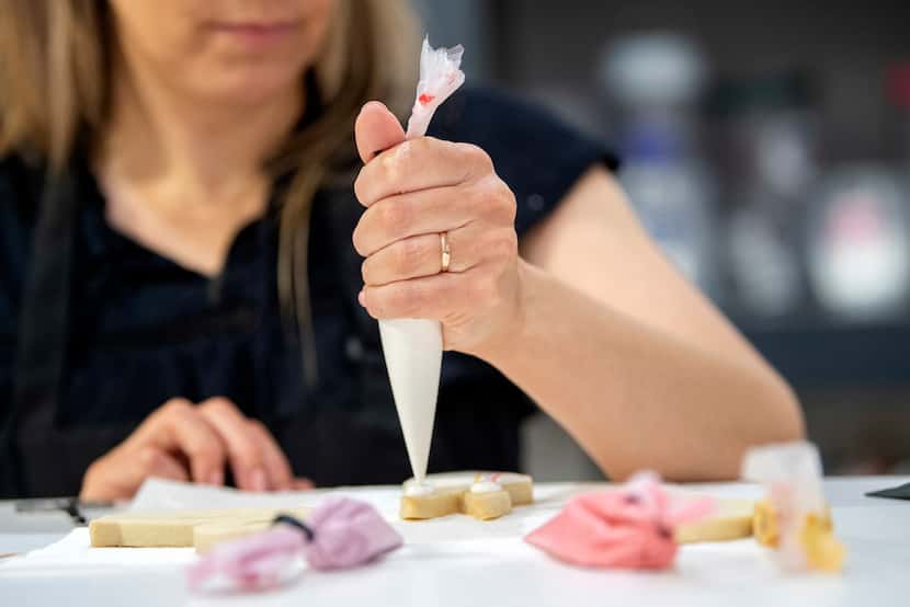 Jennifer Pedersen, owner and operator of A Dancing Baker, adds icing to a cookie as she...