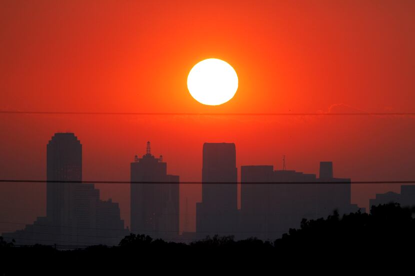 The sun sets beyond a humid city skyline following the storm that passed through Dallas,...