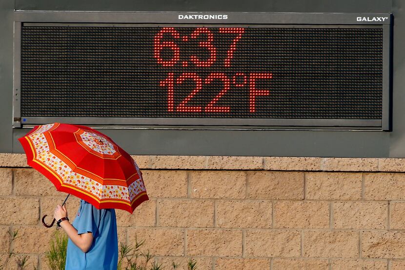 A pedestrian uses an umbrella to get some relief from the sun as she walks past a sign...