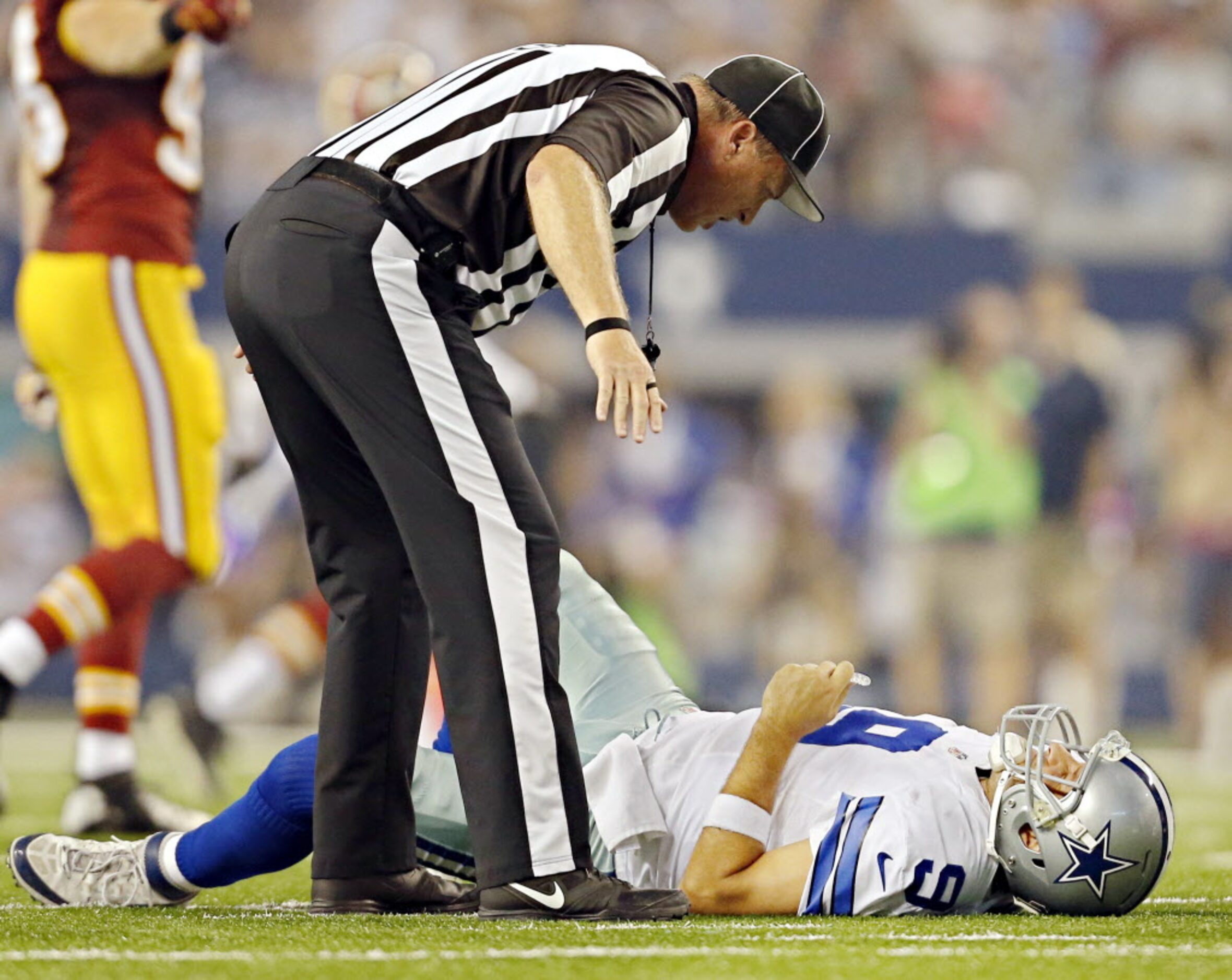 A game official leans over an injured Dallas Cowboys quarterback Tony Romo (9) after he...