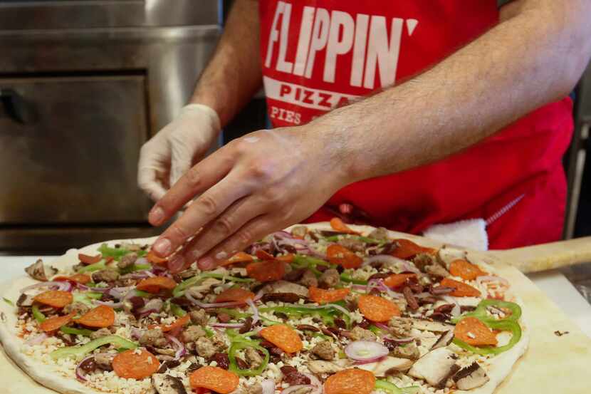 Carlos Osuna puts the finishing touches on a 18-inch pizza, Flippin' Pizza Thursday June 29,...