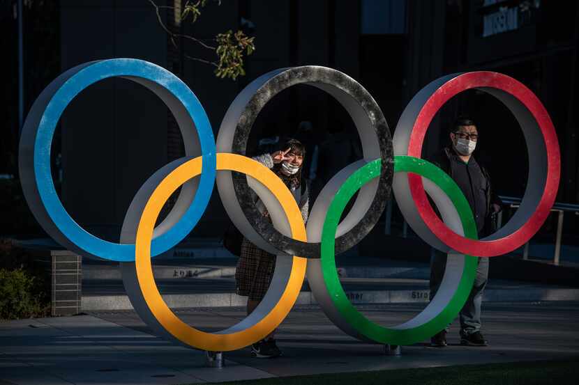 People wearing face masks pose for photographs next to Olympic Rings on March 24, 2020 in...