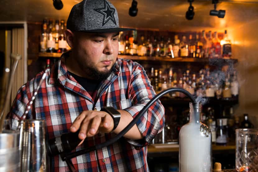 Mixologist Manny Casas at Rye in McKinney smokes cherry wood and cinnamon in a bottle while...