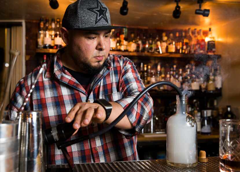 Mixologist Manny Casas at Rye in McKinney smokes cherry wood and cinnamon in a bottle while...
