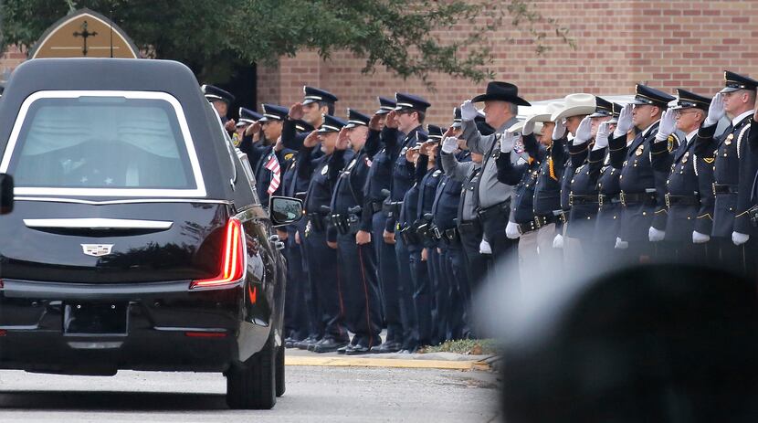 Law enforcement officers salute as the hearse drives slowly away from the church after the...