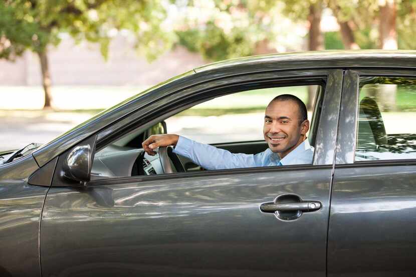A man sits in the driver's seat of a car smiling.