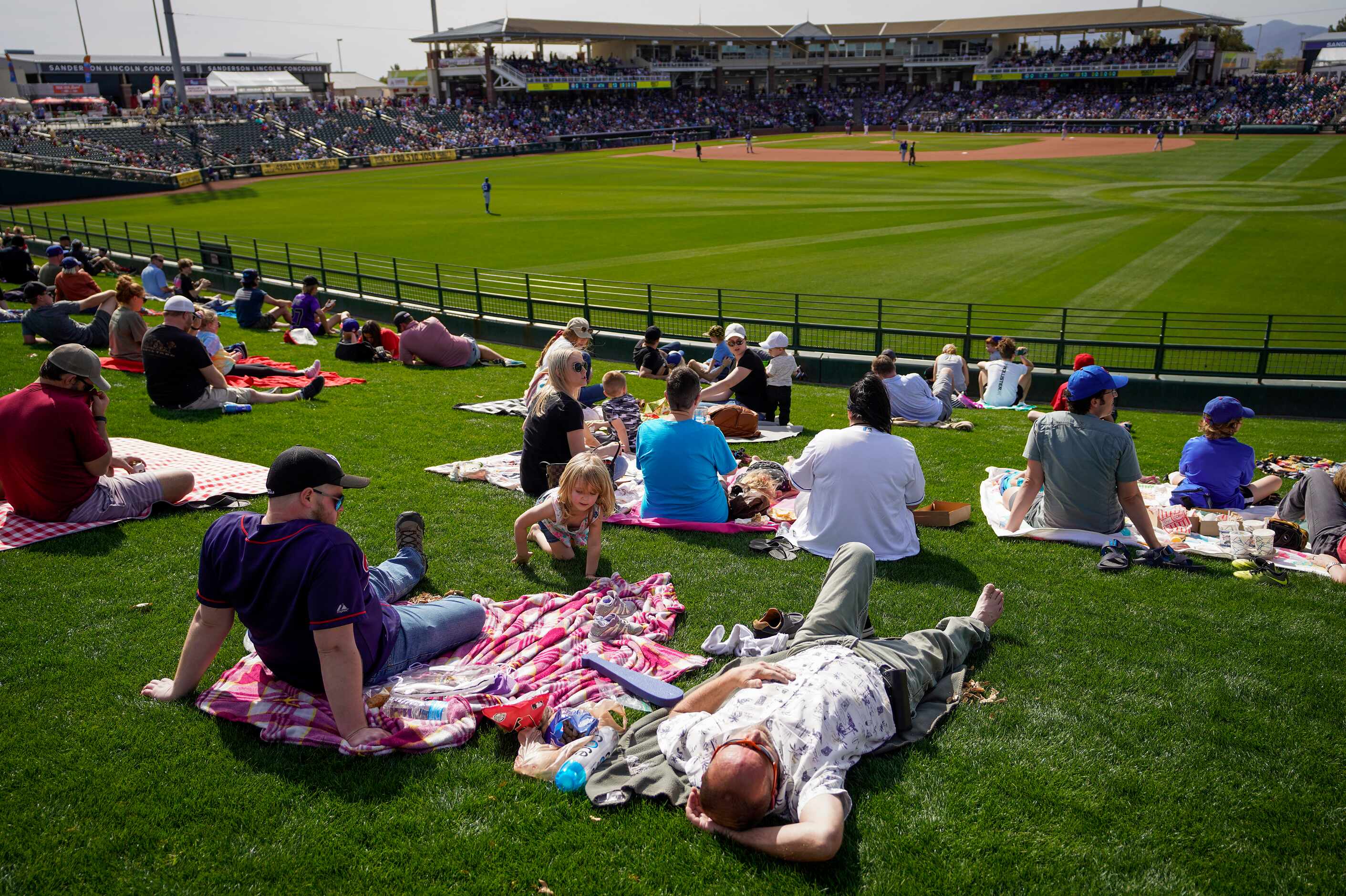 Fans relax on the outfield berm during the fourth inning of a spring training game between...