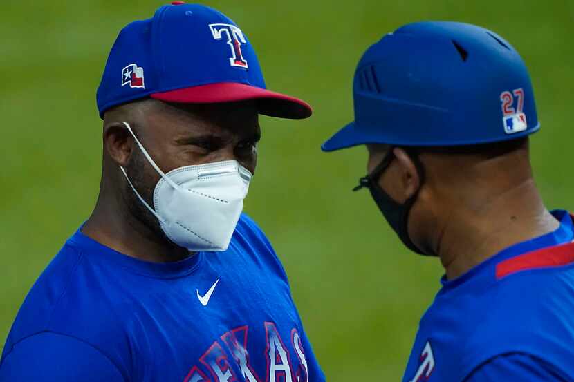Assistant hitting coach Callix Crabbe (left) wears a face mask as he talks with third base...