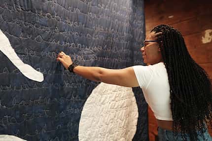 Woman touches a large mixed-media artwork that features cloth embroidered with text.