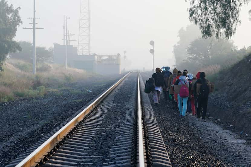 Migrantes caminan a lo largo de las vías del tren con la esperanza de subirse a un tren de...