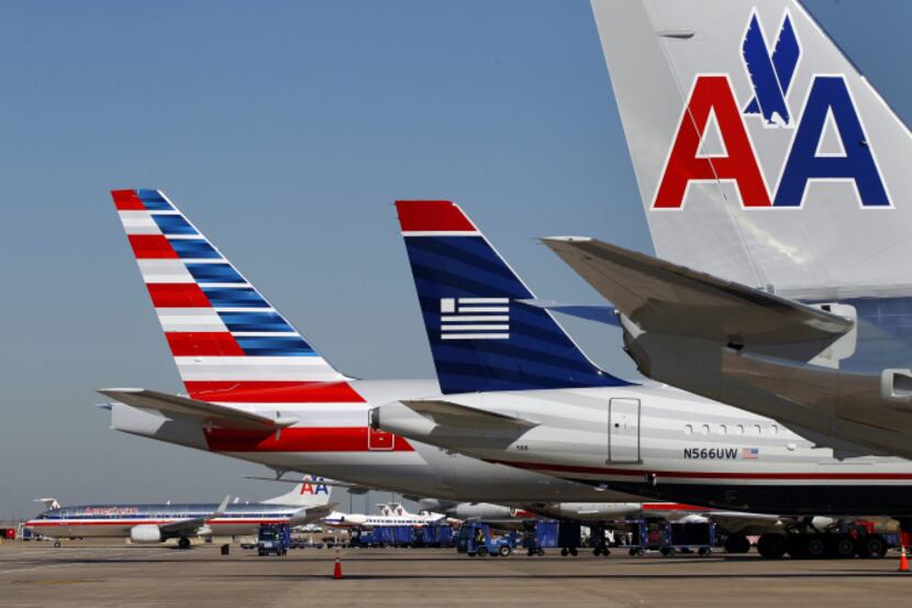 A US Airways plane is parked between two American Airlines planes, one bearing the new logo,...
