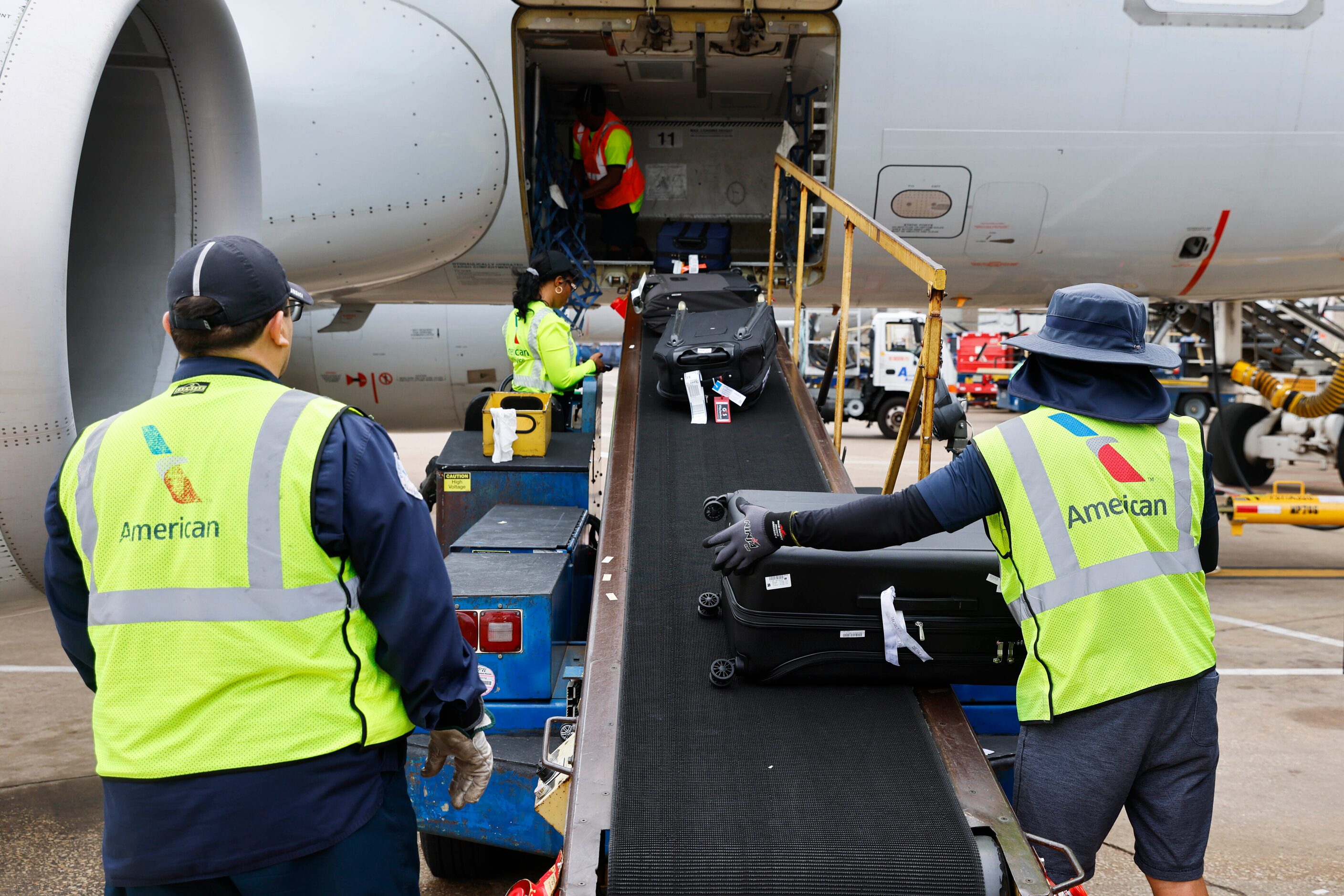 Members of the ground crew unload baggage from an American Airlines flight from Grand...