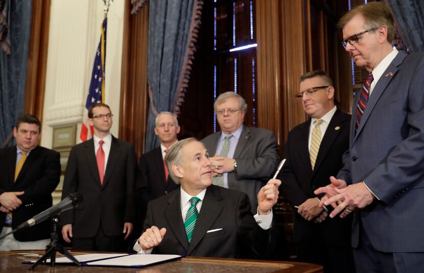 Gov. Greg Abbott (center) offers a pen to Lt. Gov. Dan Patrick (right) on Thursday after he...