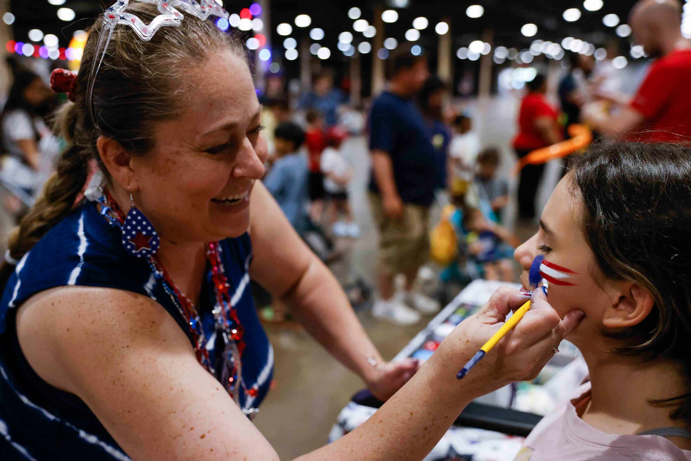Lisa Pfeifer, left, draws a face pain on Ella Gallardo, 11, of a U.S National flag during an...