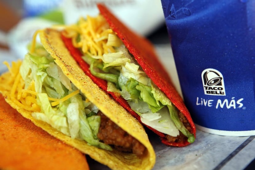 A trio of Taco Bell Doritos Locos tacos and a fountain drink are arranged for a photograph...