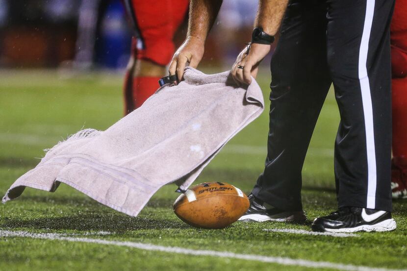 An official covers the game ball to keep it dry during a matchup between the Melissa...