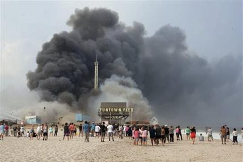 Onlookers watch from the shore as black smoke rises from a fire on the Seaside Heights, N.J....