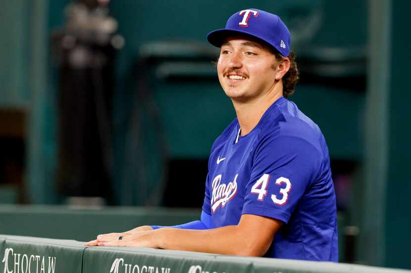 Texas Rangers relief pitcher Owen White (43) smiles as he sits in the dugout before making...