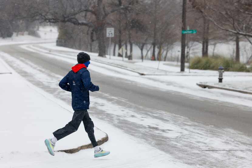 A runner crosses a snow covered Garland Road near White Rock Lake, Monday, Jan. 15, 2024, in...