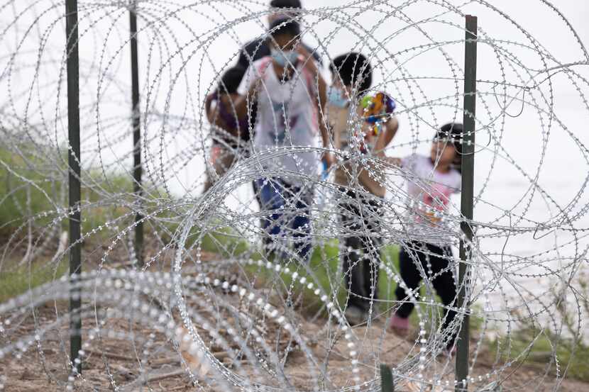 Migrants with children walked by razor wire fencing after crossing the Rio Grande River from...