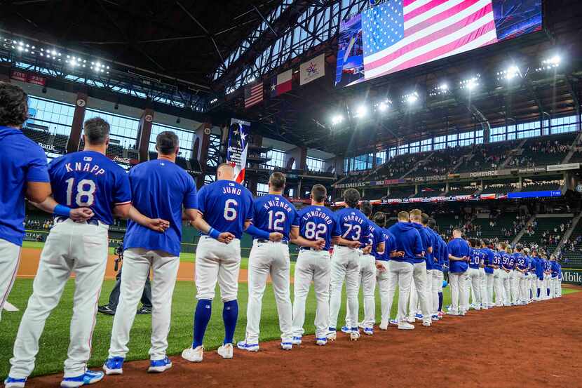Texas Rangers players stand for the national anthem before an exhibition baseball game...