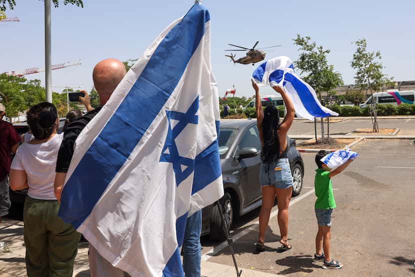 People wave Israeli flags to helicopter carrying hostages who were kidnapped in a Hamas-led...