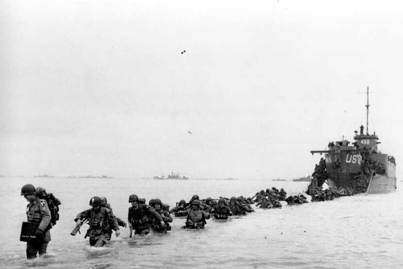 U.S. reinforcements wade through the surf from a landing craft in the days following D-Day...