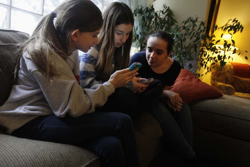 Kate McClintock, 12, left, Kate Green, 13, and Lilly Bond, 13, look at their smartphones at...