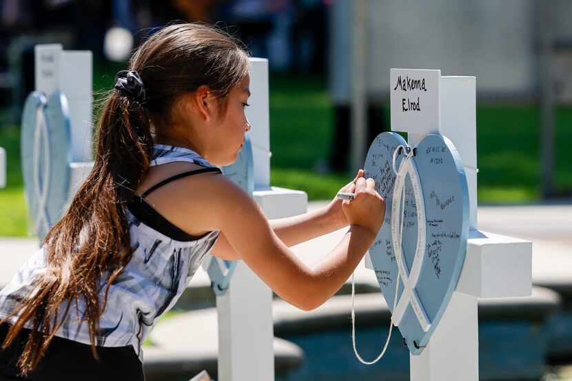 Emma Trevino, 7, writes “I love you” on a cross in memory of ten-year-old Makenna Lee Elrod...