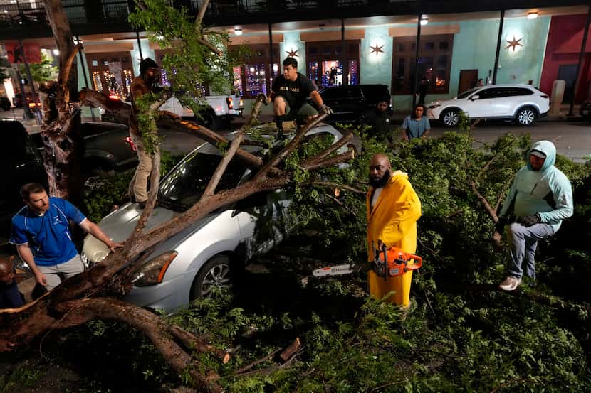 Rapper Trae tha Truth, in yellow, cuts fallen tree limbs on top of a car in the aftermath of...