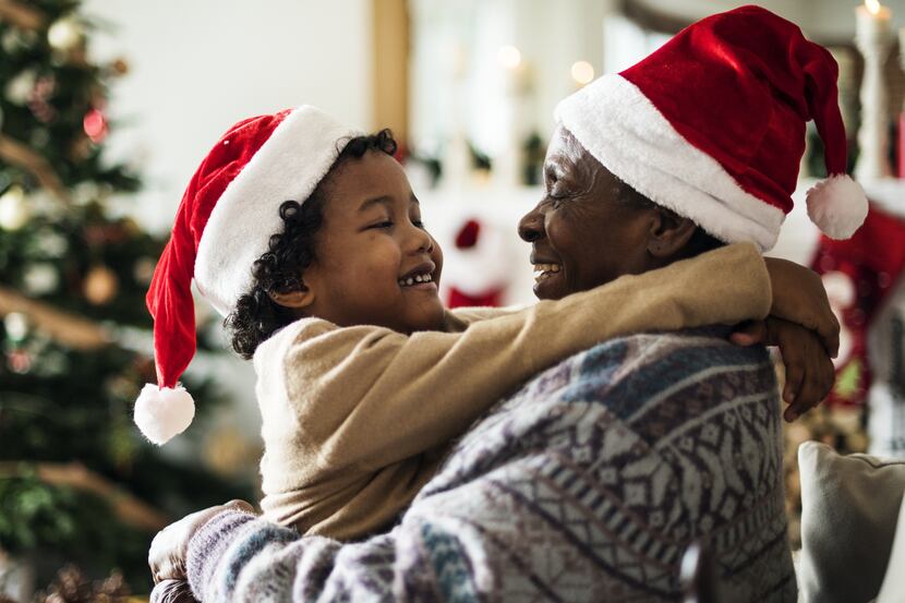 A parent and child hug while wearing Santa hats with a Christmas tree in the background.