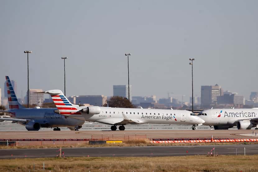 An American Eagle and American Airlines planes make their way toward the runway before...