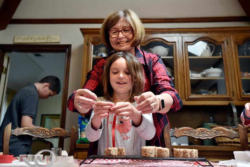 Tina Dempsey helps her grandchild Tatum Dempsey, 8, tie a ribbon to a Christmas ornaments of...